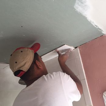 Person applying compound to a ceiling corner with a trowel, wearing a baseball cap.