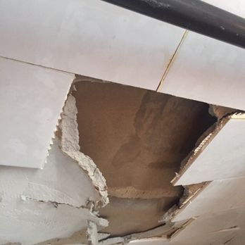 Damaged ceiling with a large hole, exposing the interior. White tiles are broken and cracked.