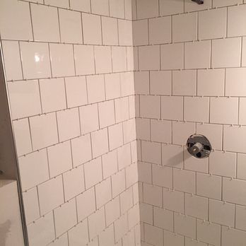 White tiled shower stall with a shower head and faucet.
