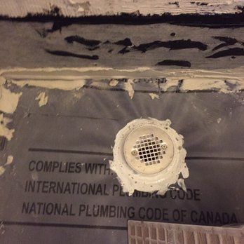 Shower drain with a metal grate set in concrete, against a dark waterproof membrane.
