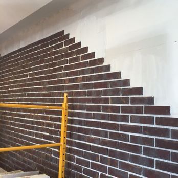 Brick veneer wall under construction; dark red bricks, white grout, yellow scaffolding.