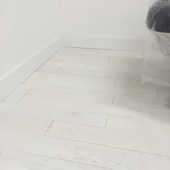 White-painted wooden floorboards and baseboards against a white wall; partially visible, plastic-covered chair.