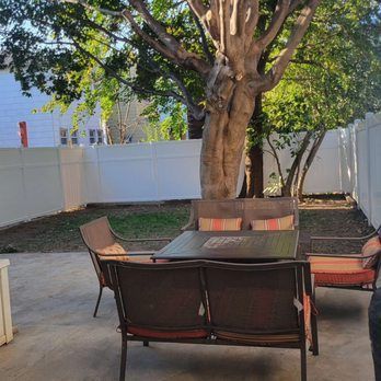 Patio with outdoor furniture, large tree, and white fence in a backyard.