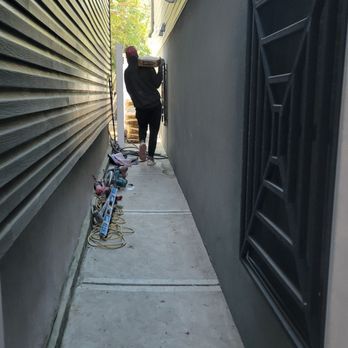 Person carrying a toolbox in a narrow alleyway between buildings, tools and cords on the ground.