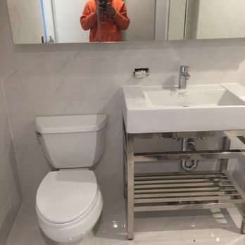 Modern bathroom with white toilet, sink, and chrome fixtures. Mirror and tiled walls. Someone taking a photo.