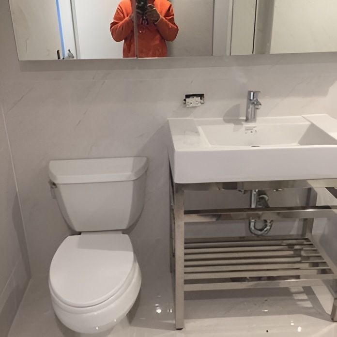 Bathroom with white toilet, sink, and chrome fixtures. Mirror and white tile walls.