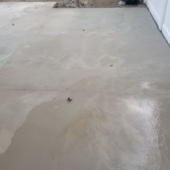 Newly poured, smooth, gray concrete patio with water marks and a few small debris.
