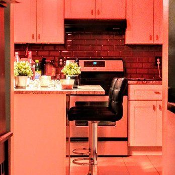 Small kitchen with white cabinets, red brick backsplash, and a black stool.