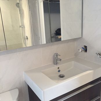 Modern bathroom with white sink, mirror, and shower. Dark brown cabinet.
