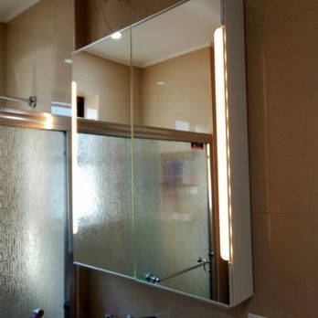Bathroom mirror with built-in light, reflecting shower and beige wall.