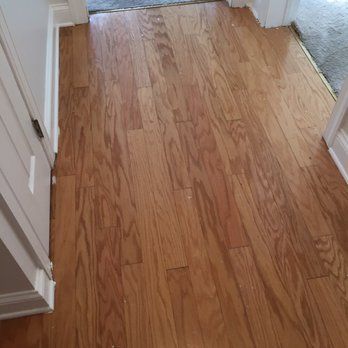 Hardwood flooring, light brown, in a hallway. White doorframes and doorway edge with carpet visible.