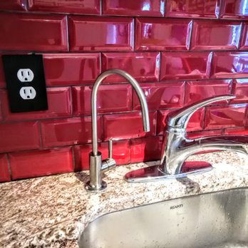 Stainless steel kitchen faucet and water dispenser on a granite countertop, with red subway tile backsplash and a black outlet.