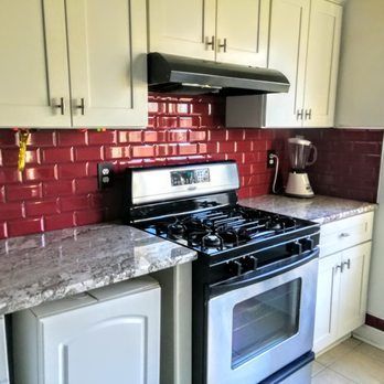 Kitchen with red backsplash, stainless steel stove, and white cabinets.