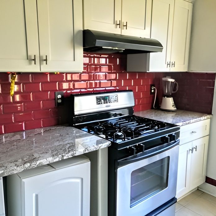 Kitchen with red subway tile backsplash, stainless steel stove, white cabinets, and a blender.