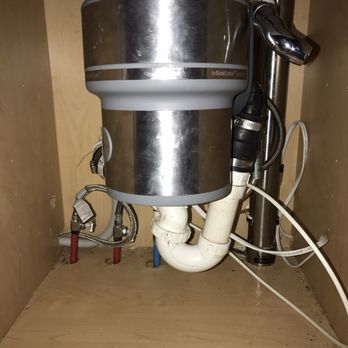 Garbage disposal unit under a kitchen sink, with plumbing and electrical connections visible.