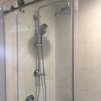 Shower with a glass door, silver fixtures, and a handheld showerhead. Light-colored tile.