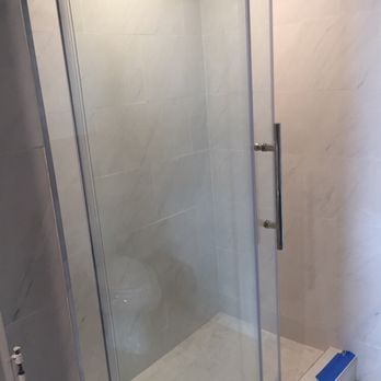 Shower stall with glass door and silver handle, white tile walls.
