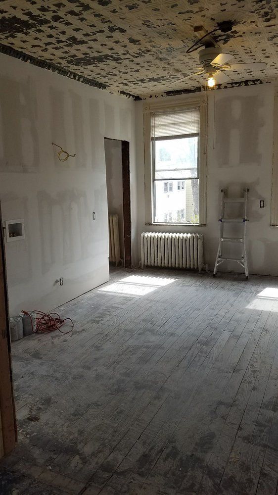 Room undergoing renovation with damaged ceiling, old window, and wooden floor.