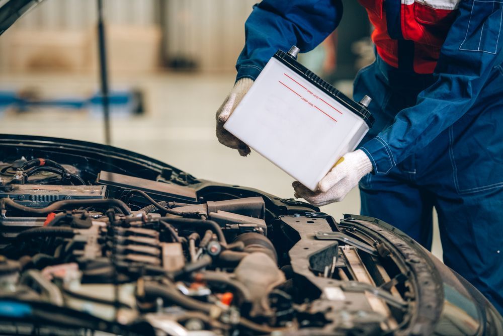 A Mechanic in Blue Coveralls Holding a Car Battery — O'Toole Automotive In Tuggerah, NSW