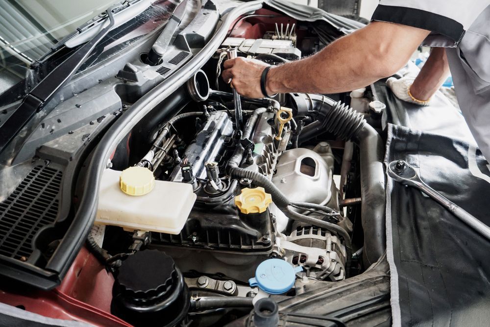 A Mechanic Uses a Tool to Work on the Engine Inside the Open Hood of a Car — O'Toole Automotive In Tuggerah, NSW