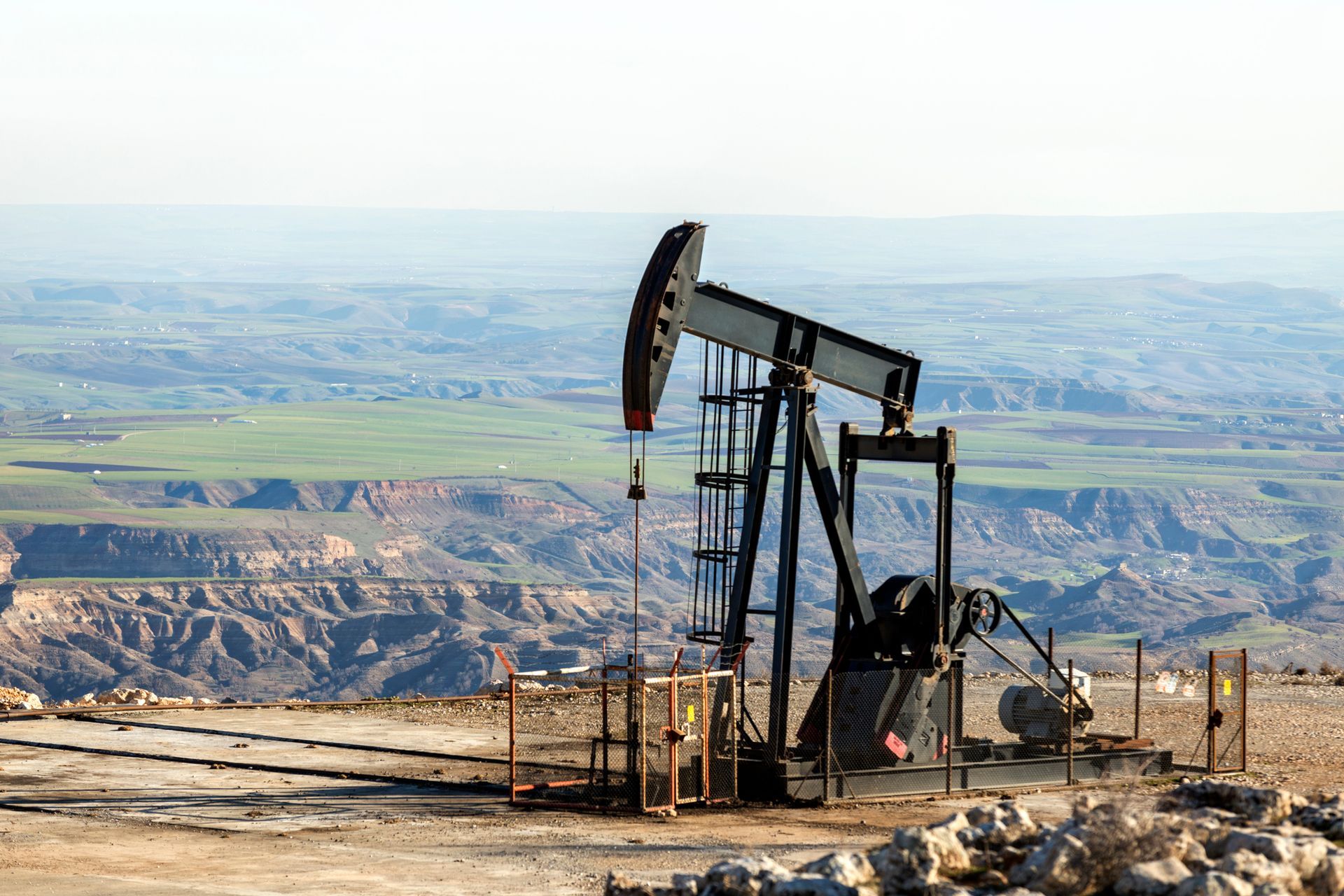 An oil pump is sitting on top of a hill in the middle of a desert.