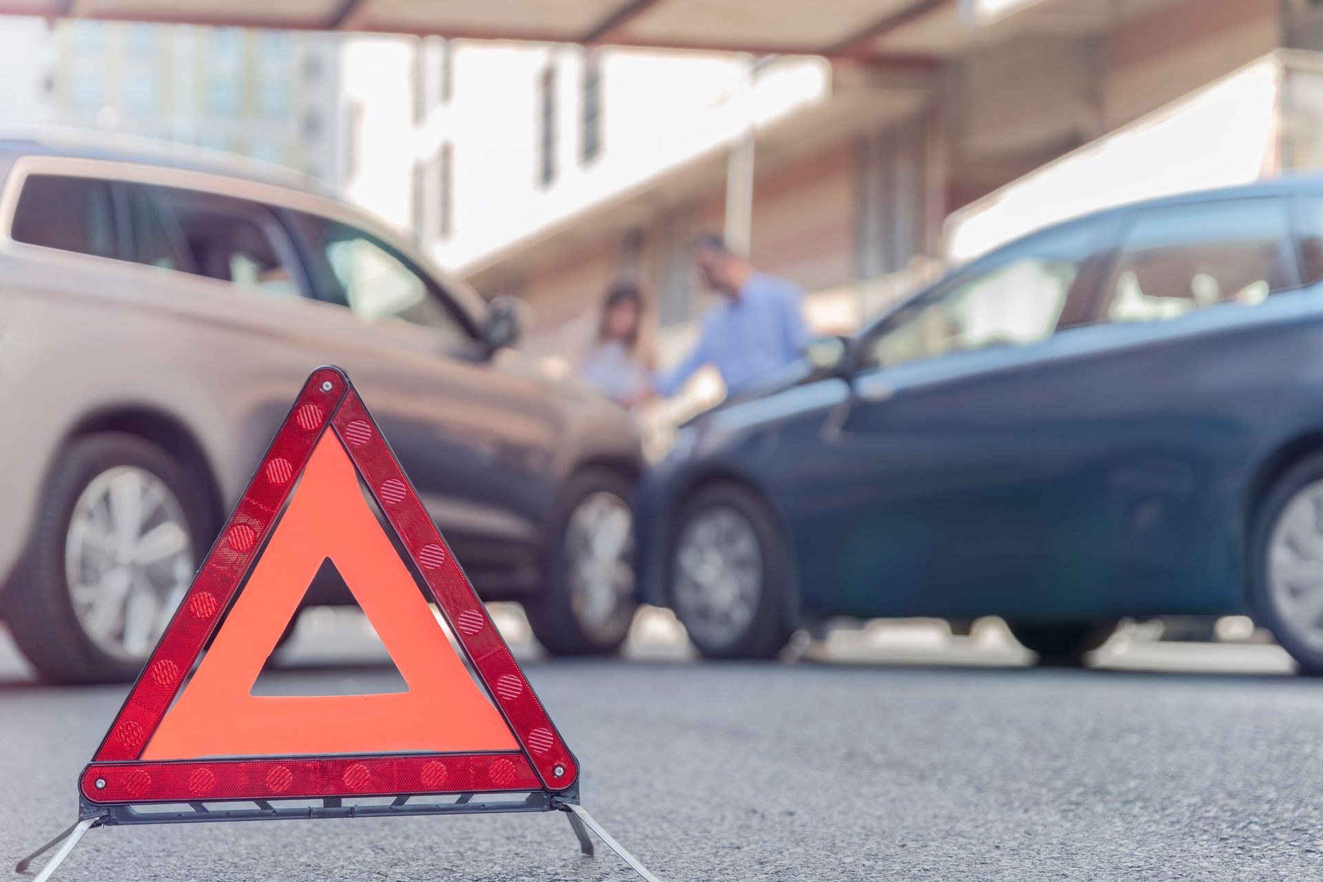 A warning triangle is sitting on the side of the road in front of a car accident.