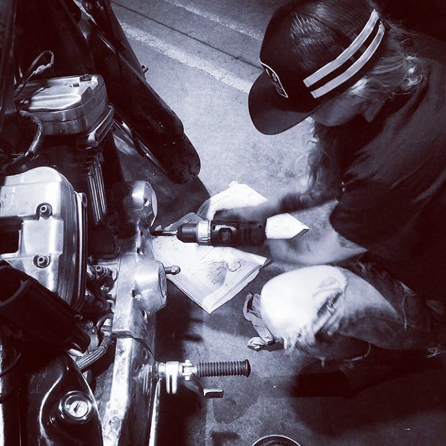 Ms Fix It working on a motorcycle engine with a power drill indoors.