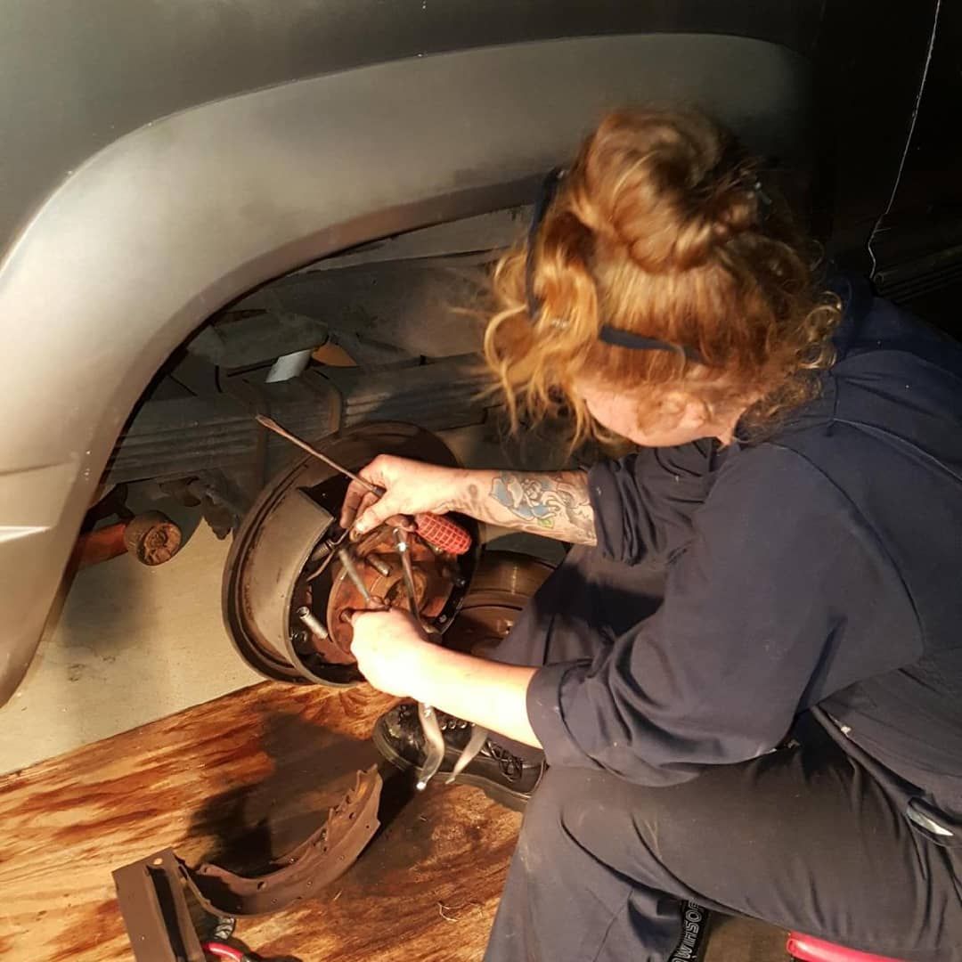 Teresa Ley, Woman working on a car's brake system, dark clothing, fair skin, light red hair, tool in hand.