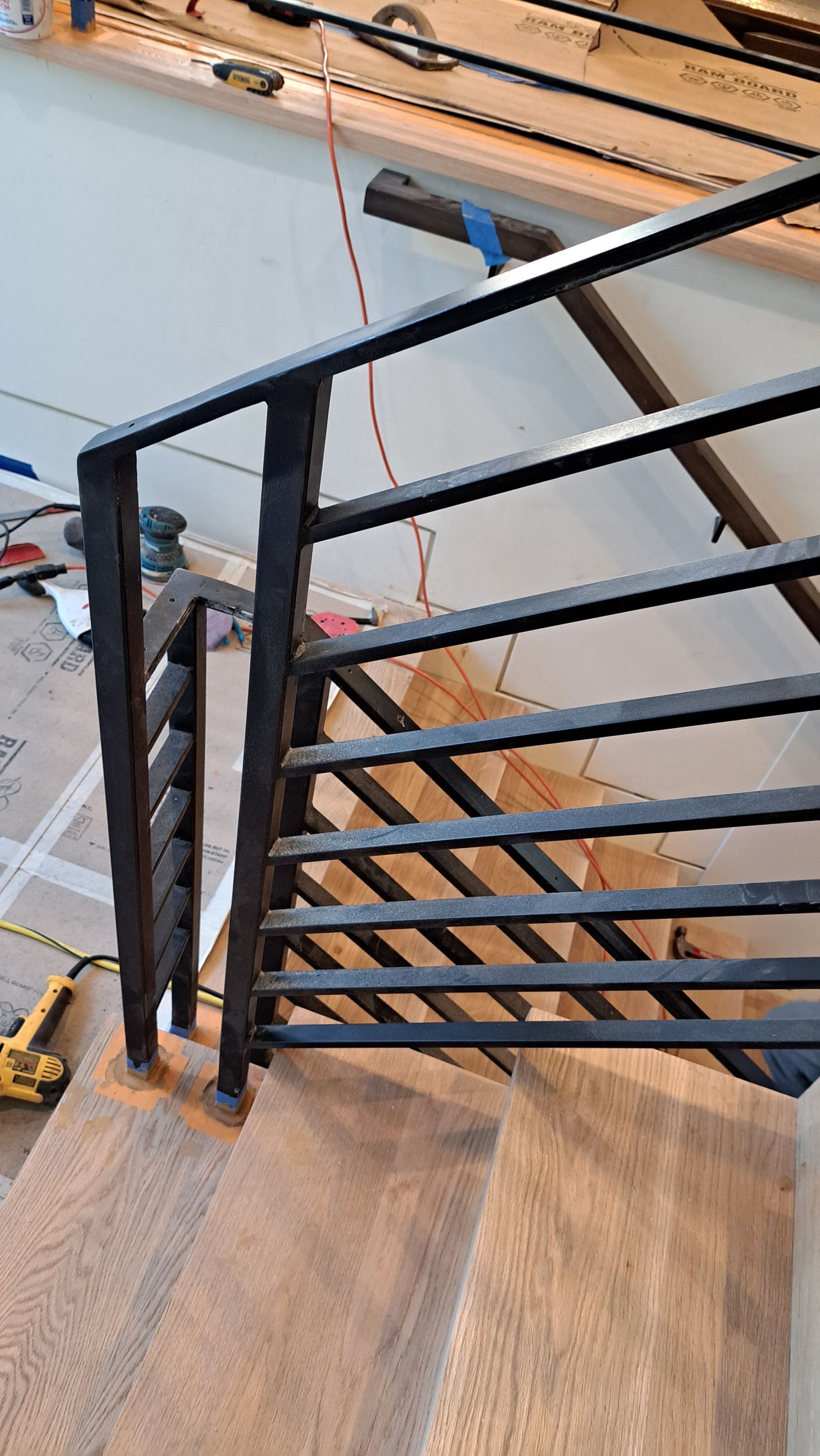 Black metal stair railing installed on wooden steps. Construction debris in the background.