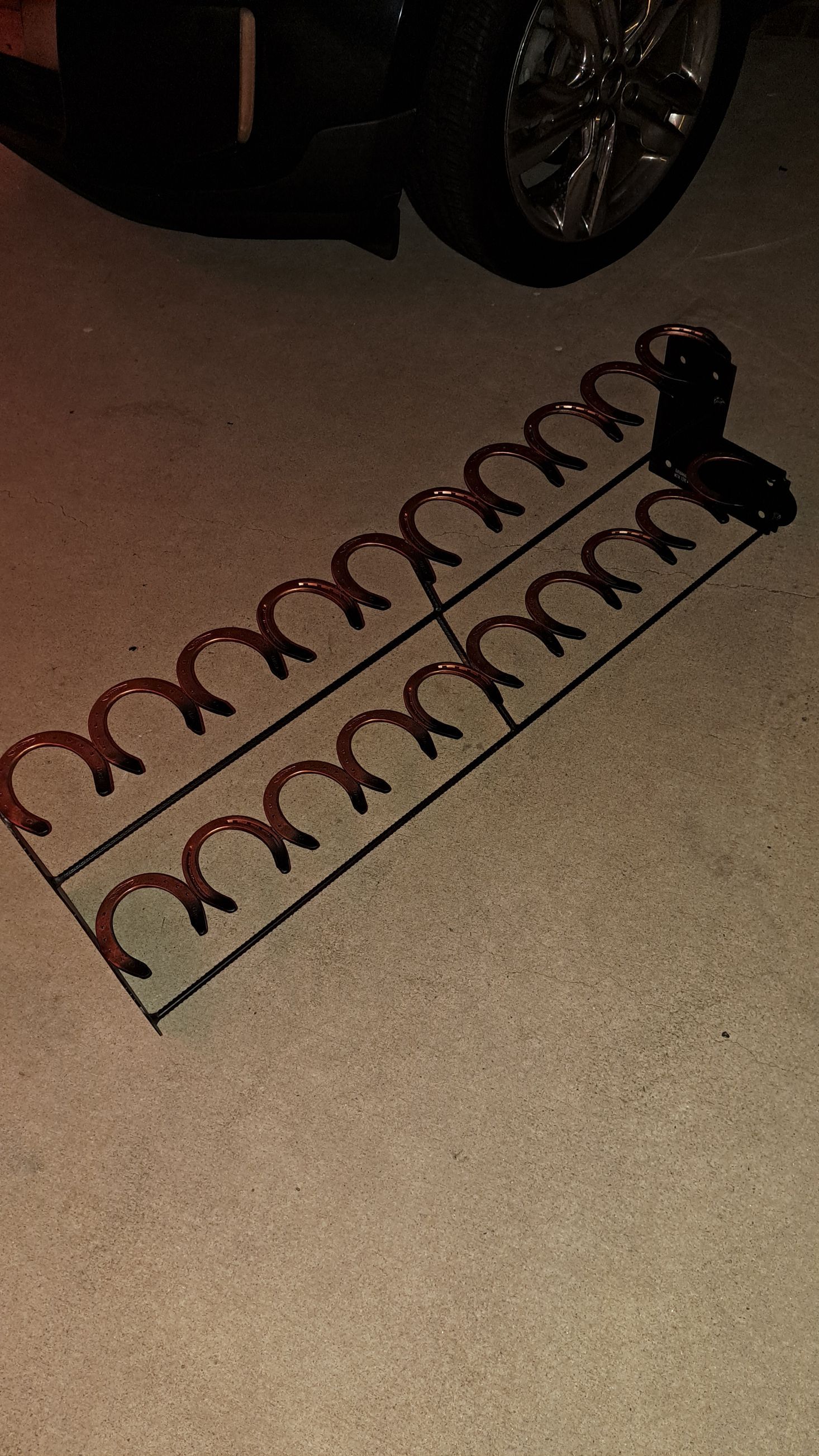 Black metal horseshoe-shaped boot rack with two cup holders, on a concrete surface.