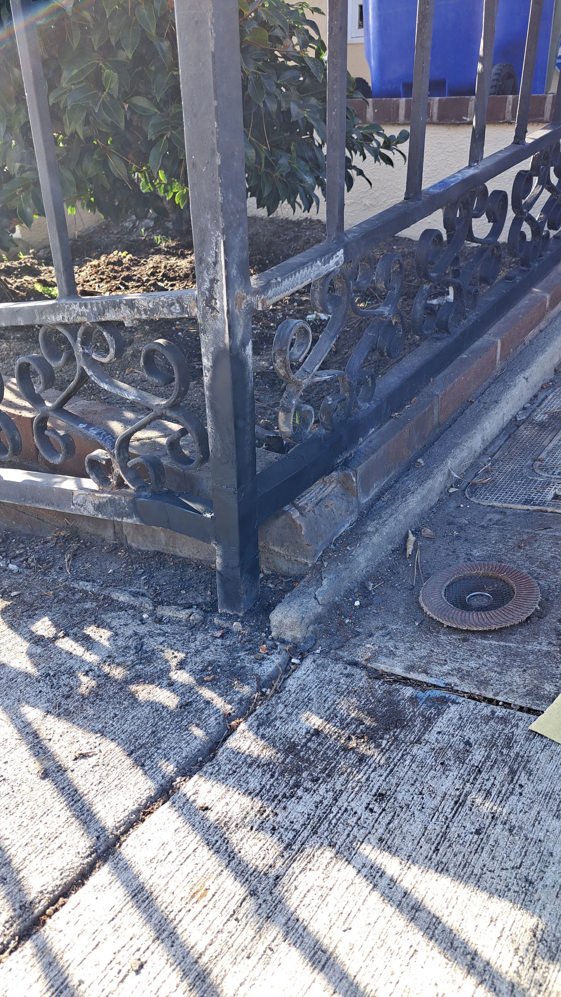 Iron fence post partially embedded in concrete, with ornamental details; low angle.