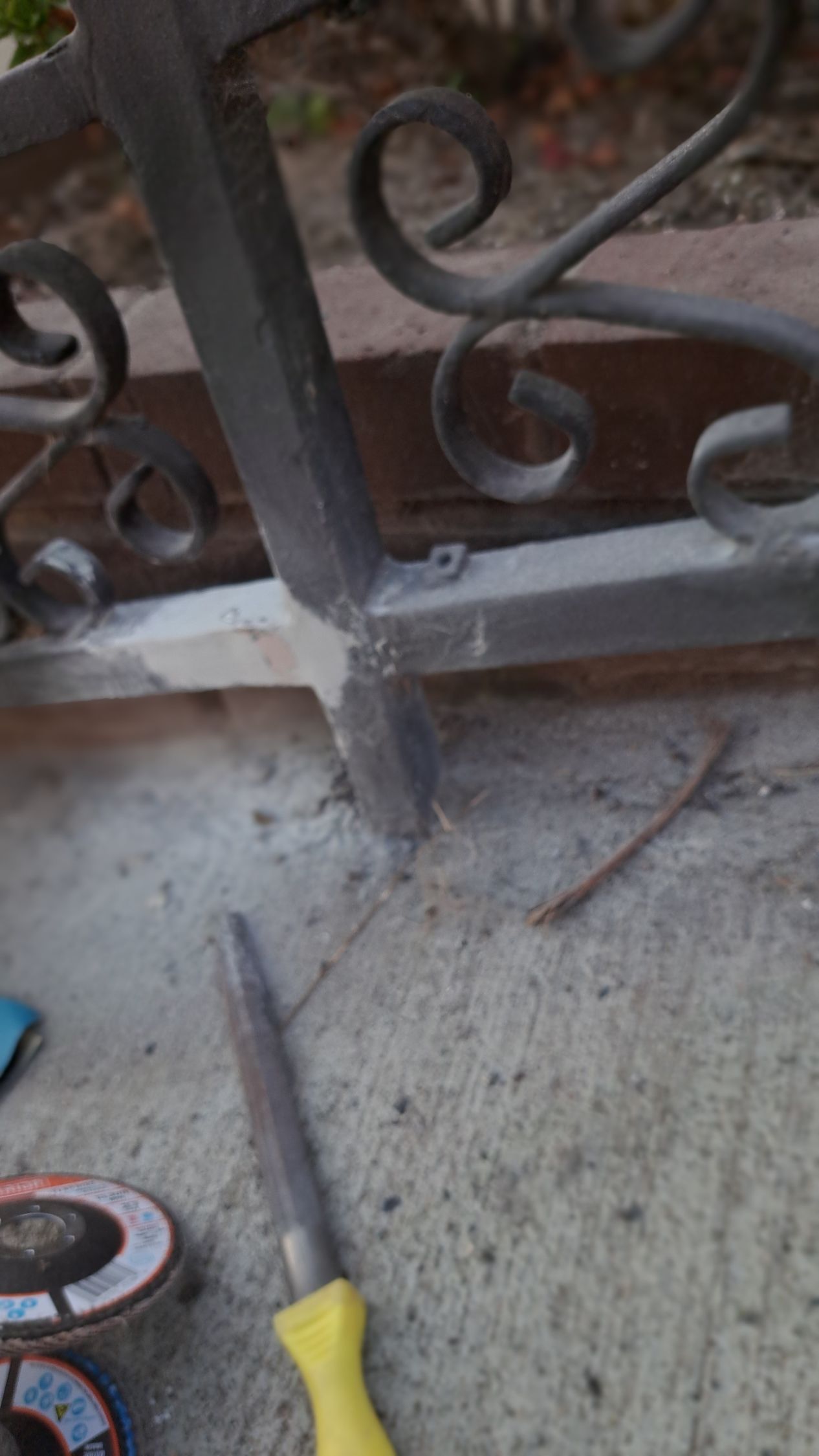 Metal gate being worked on, sitting on concrete. A file is nearby.
