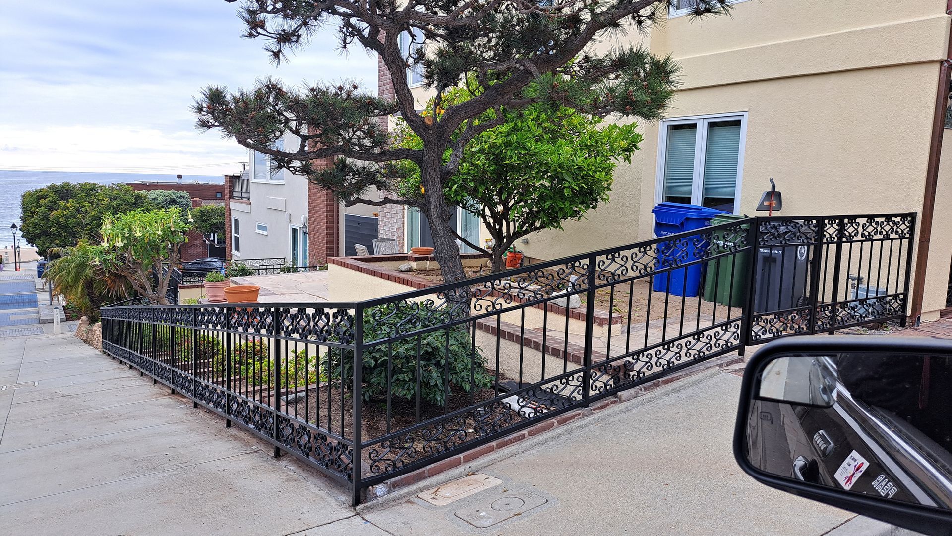 Wrought iron railing and a tree in front of a house on a sloped street with ocean view.