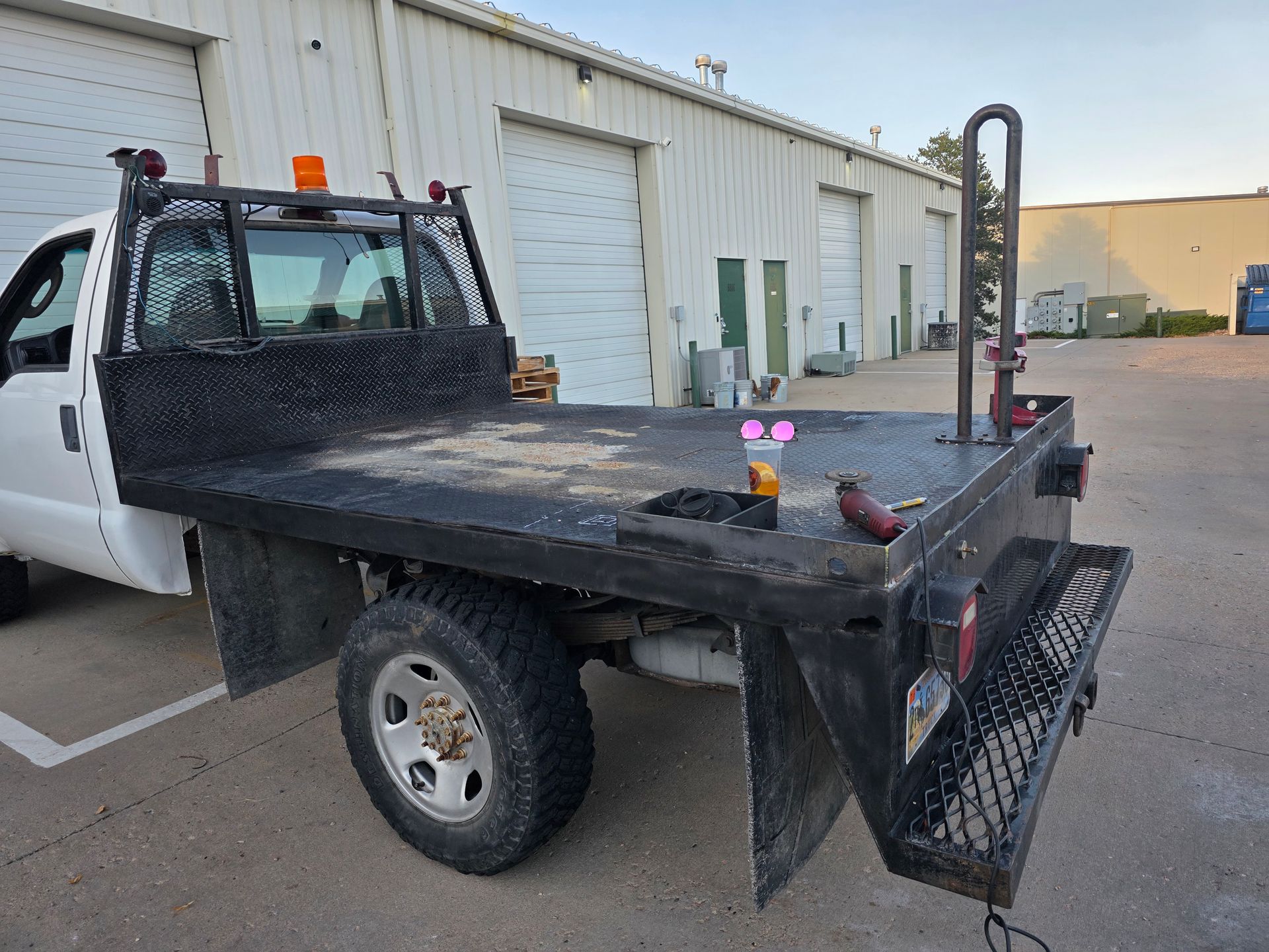 White work truck with a flatbed, parked in front of a building with garage doors.