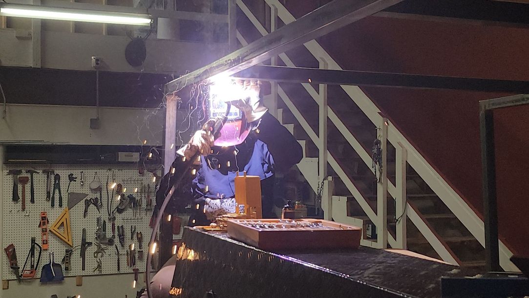 Welder wearing a mask working on a metal frame, sparks flying.
