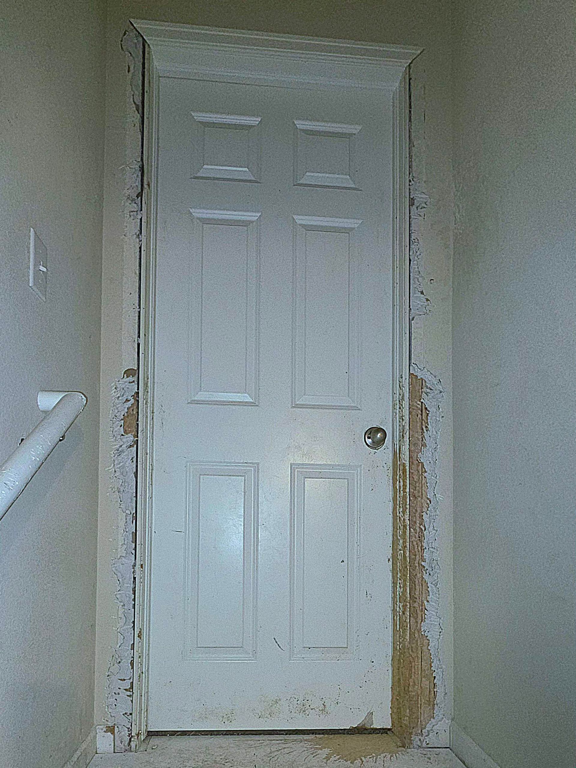 White interior door with peeling paint and surrounding damage in a hallway.