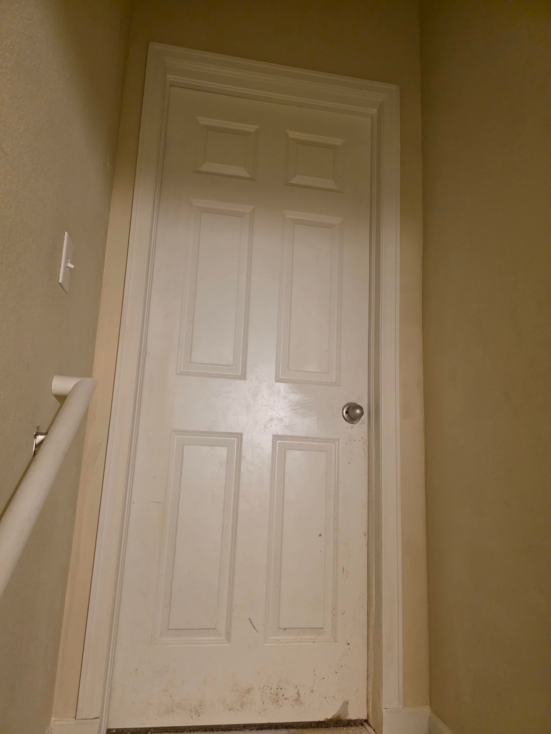 White door in a hallway with a stairwell visible on the left.