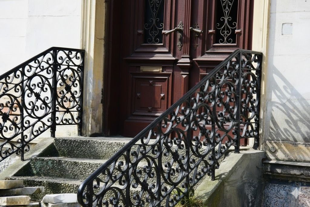 Ornate black ironwork handrails on steps leading to a dark wooden door.