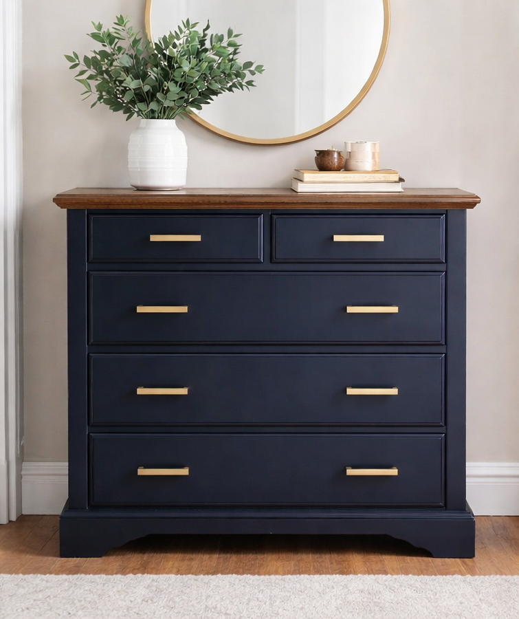 Navy blue dresser with gold hardware and brown top, topped with decor and a mirror.