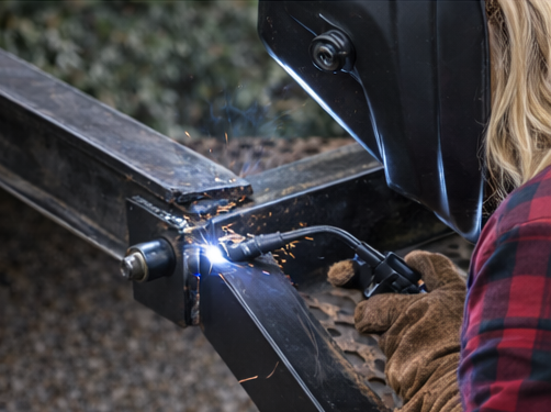 Welder in plaid shirt welding metal with sparks flying.