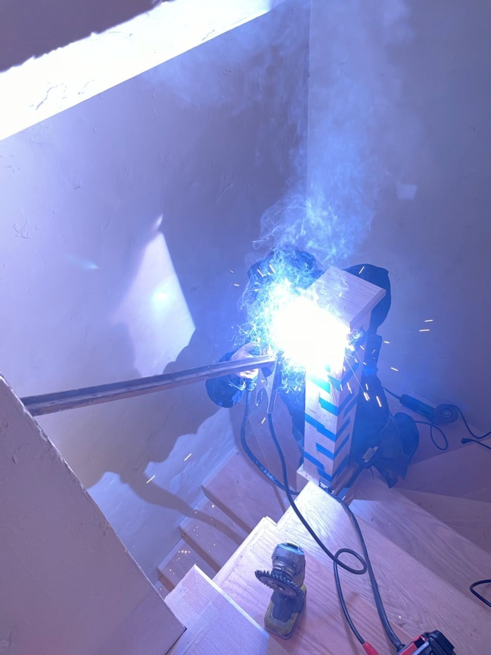 Person welding metal on stairs, bright blue light and smoke visible.