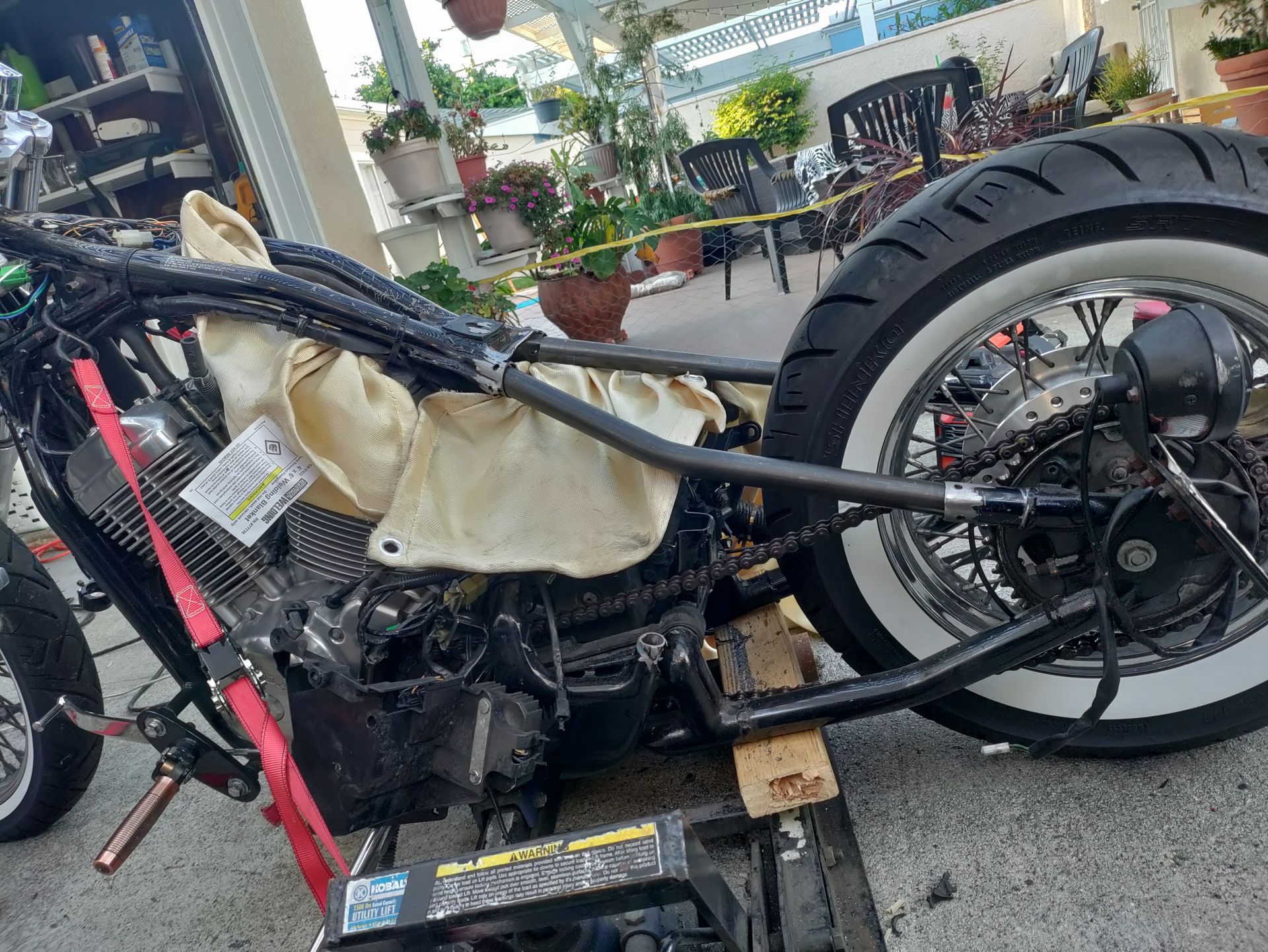 Black motorcycle frame with white-walled tire, under construction outdoors.