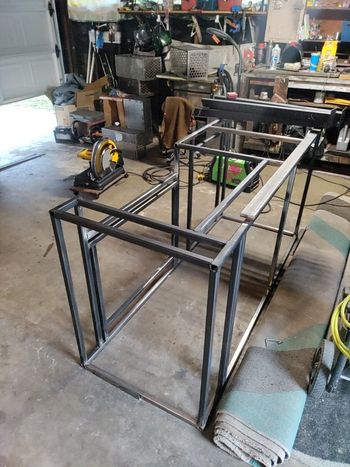 Metal frames of a structure under construction in a workshop. A chop saw is nearby.