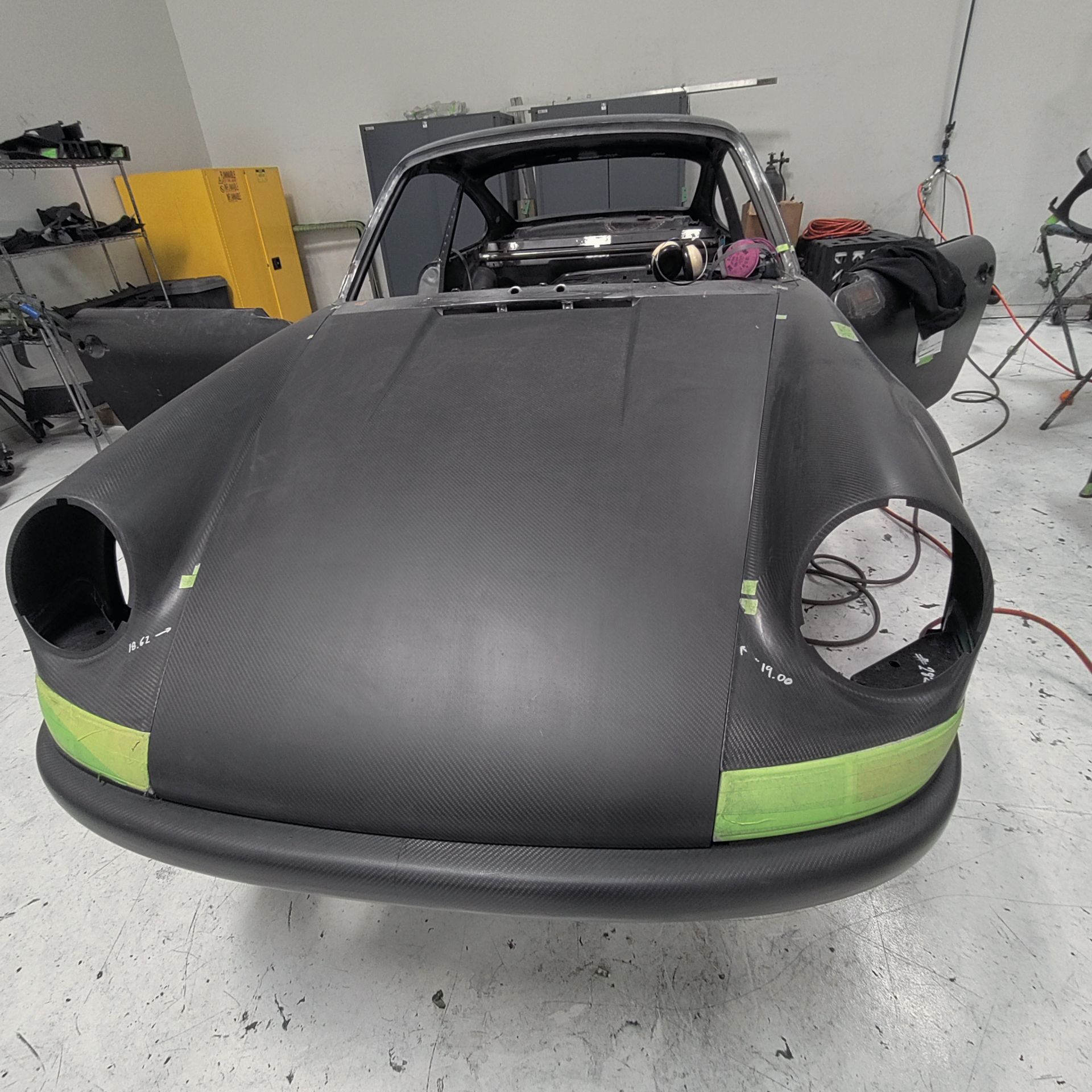 Black Porsche car body with green tape in a garage setting. Ms Fix It