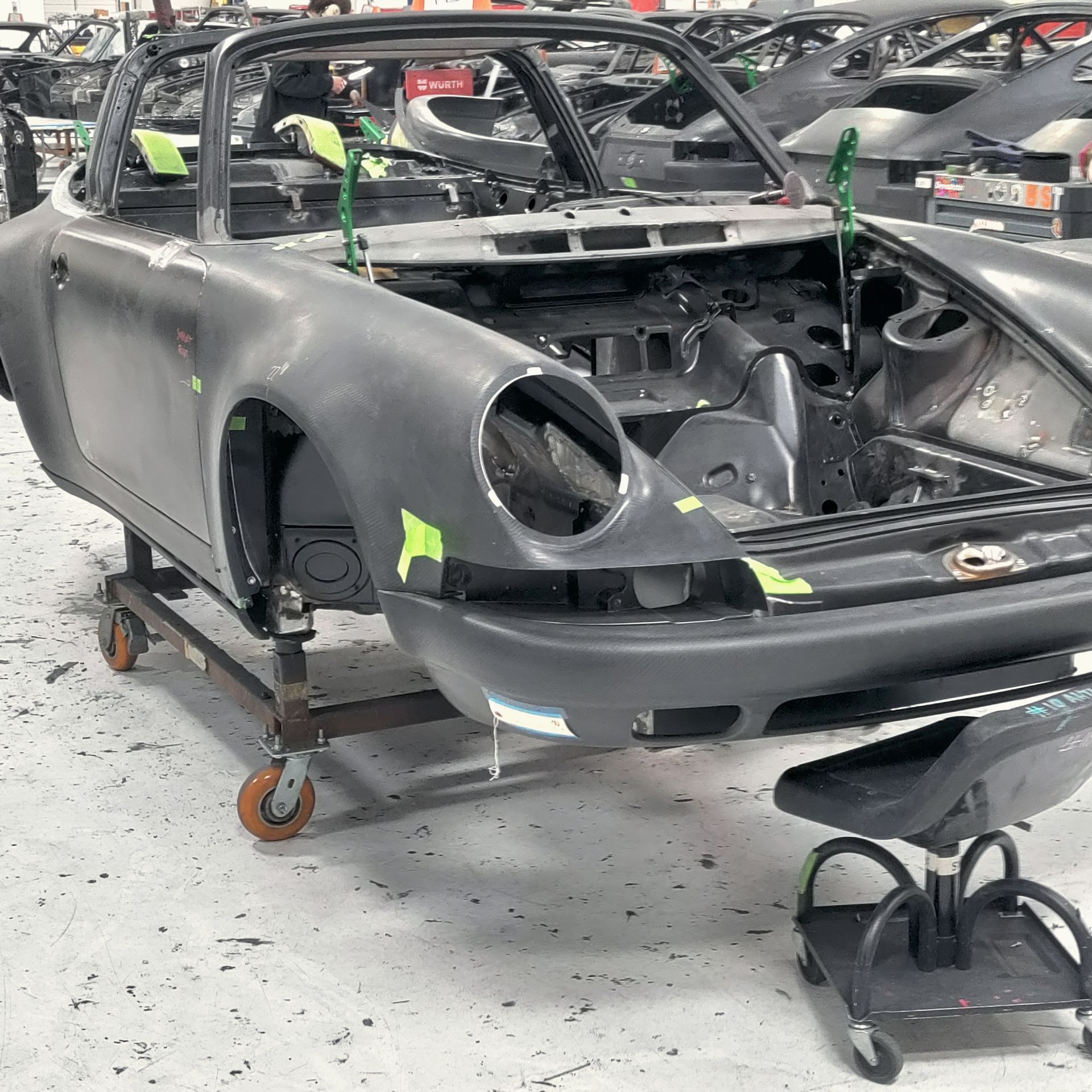 Partially assembled gray Porsche 911 convertible body on a rolling cart in a workshop.