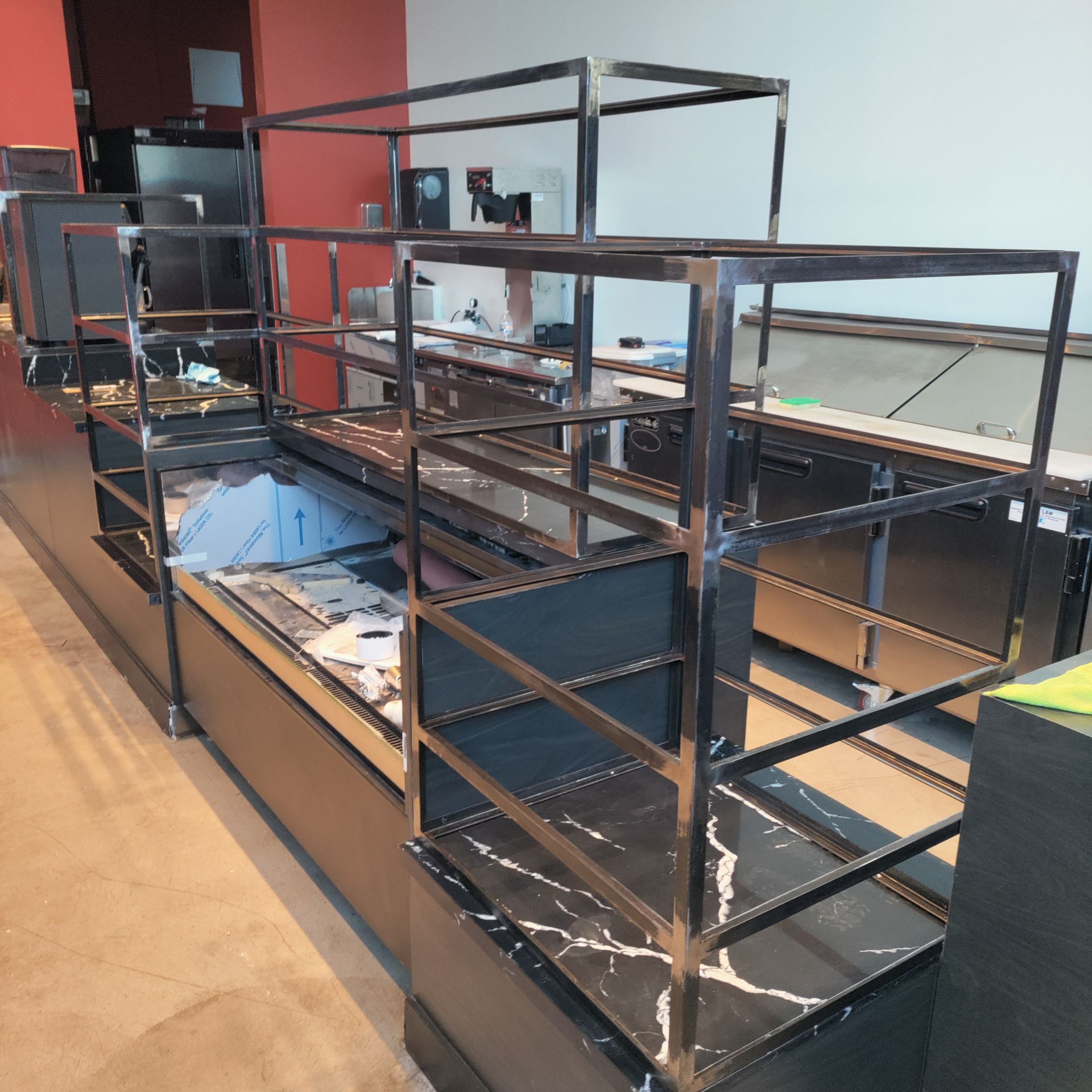 Empty metal display shelves in a store, with black countertops and red wall in the background.
