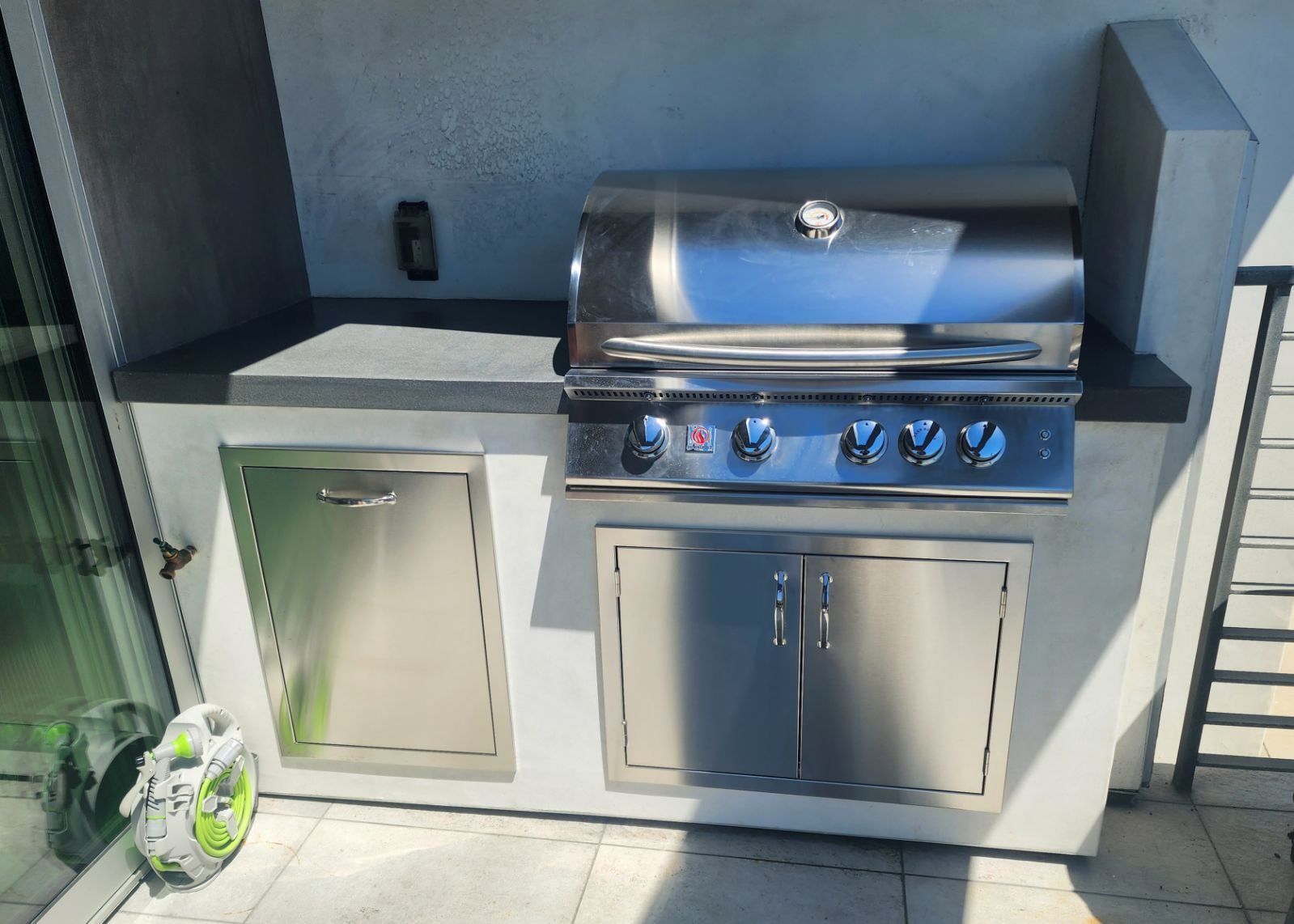 Outdoor stainless steel grill built into a concrete countertop with storage, on a patio.