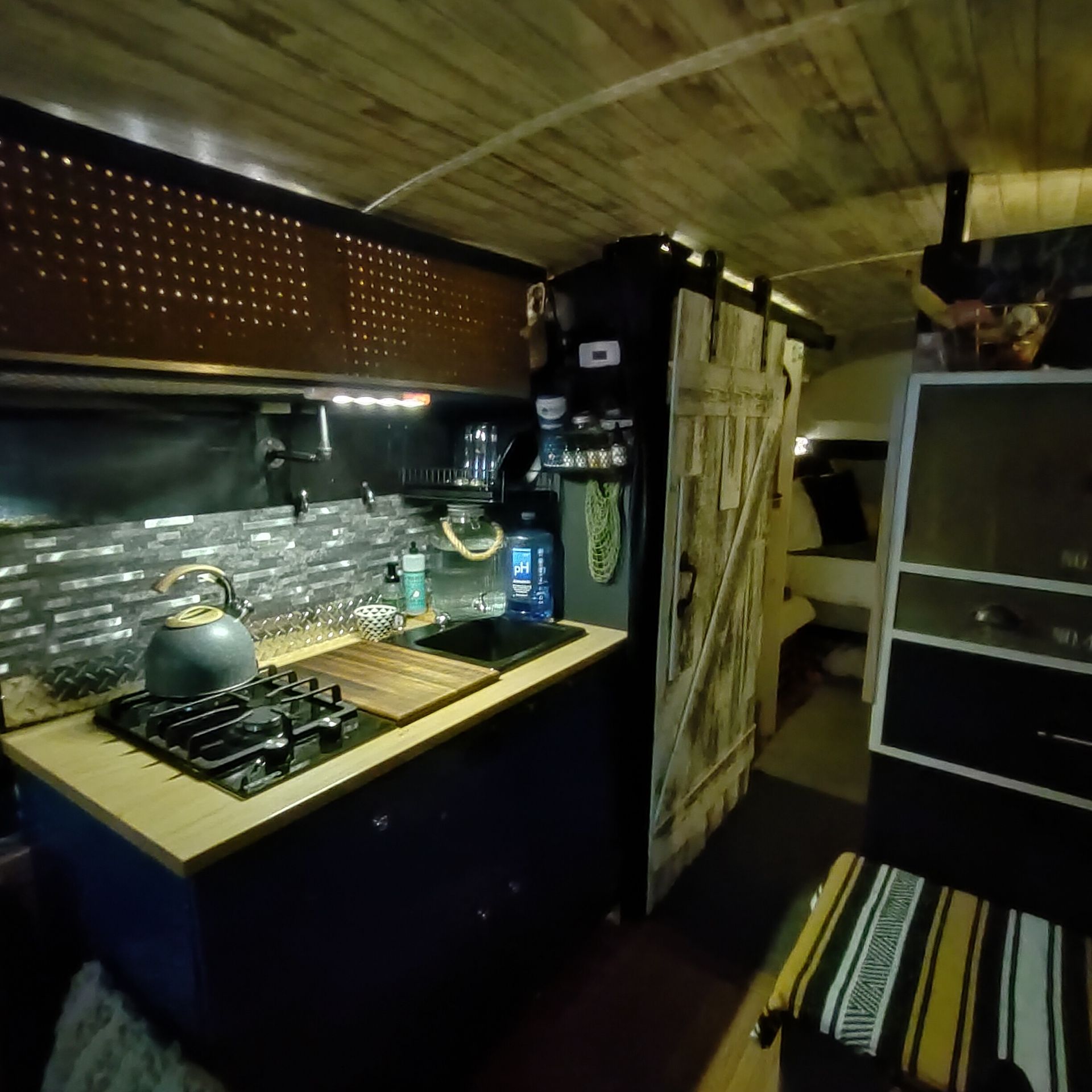 Interior of a camper van kitchen with dark blue cabinets, wood accents, and a barn door.