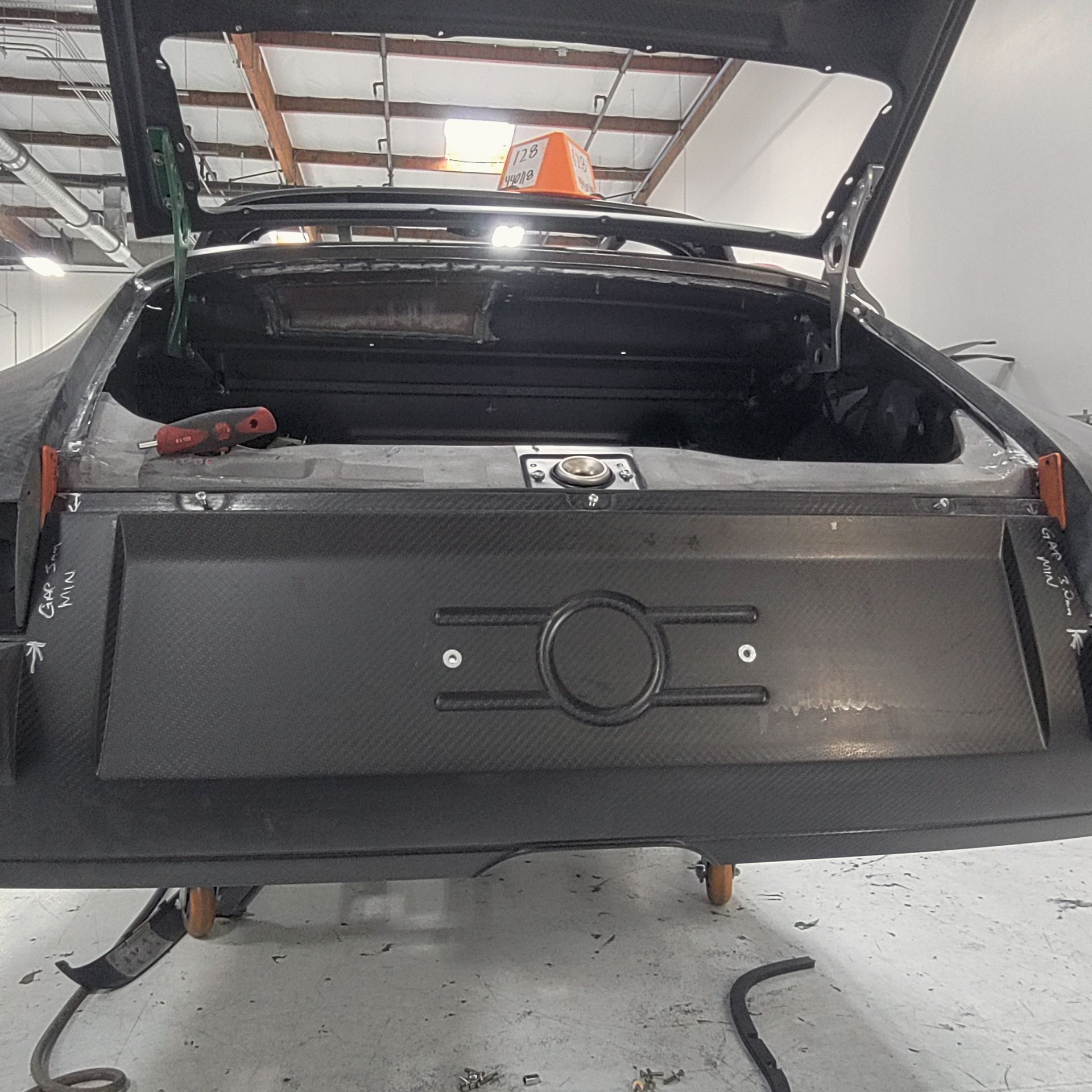 Rear of a black car with the trunk open, revealing a carbon fiber panel.