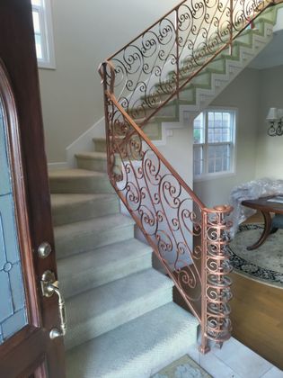 Ornate wrought-iron banister with spiral staircase, carpeted stairs, and a wooden front door.
